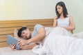 Asian man use taplet on bed, ignoring the girlfriend sitting next to him