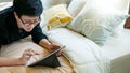 Asian man using digital tablet on bed in bedroom Royalty Free Stock Photo