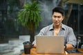 An Asian man is using his laptop, working on his work, and sitting at a coffee shop Royalty Free Stock Photo