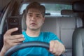 Asian man using mobile smart phone and reading messages while driving a car. Concept of negligence, dangerous behavior and Royalty Free Stock Photo