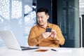 Asian man using phone in modern office, typing message and reading news while sitting at desk, businessman at work Royalty Free Stock Photo