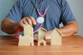 Asian man using stethoscope checking wooden model home on wood floor Royalty Free Stock Photo