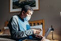 Asian man weared medical mask. Sitting and using laptop in bedroom