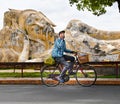 Mask wearing man cycling infront of Buddha statue