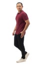 Asian man wearing maroon red shirt black denim and white shoes, walking forward, side view, happy confidence expression. Full body Royalty Free Stock Photo