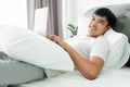 Asian man in white t-shirt laying on bed using laptop computer in bedroom