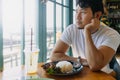 Asian man in white t-shirt waiting for someone to meet at the restaurant with Thai stir fried pork with rice. Royalty Free Stock Photo