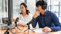 Asian Man and woman podcasters in headphones recording content with colleague talking to microphone and camera in broadcast studio Royalty Free Stock Photo