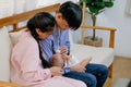 Asian man and woman take care their little baby by giving bottle milk and sit on sofa in living room of their house