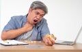 Asian man working and eating a burger on office desk and holding his neck after choking foods. Concept of a busy businessman Royalty Free Stock Photo