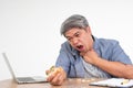 Asian man working and eating a burger on office desk and holding his neck after choking foods. Concept of a busy businessman Royalty Free Stock Photo