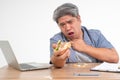 Asian man working and eating a burger on office desk and holding his neck after choking foods. Concept of a busy businessman Royalty Free Stock Photo