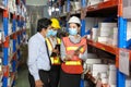 Asian manager talking to employees wearing facial mask and safety vest working in warehouse checking for the inventory