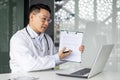 Asian mature male doctor discussing medical report on video call with laptop in office Royalty Free Stock Photo