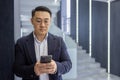 Asian mature man in business attire using smartphone in modern office setting Royalty Free Stock Photo