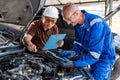 Two male car mechanics working together on the car engine at their car repair garage Royalty Free Stock Photo