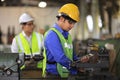 Asian mechanic worker in safety hard hat and reflective cloth is working with lathe machine inside the factory for industry