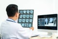 Asian man doctor holding and looking to examining x-ray of the patientÃ¢â¬â¢s skull and brain in a medical clinic at hospital Royalty Free Stock Photo