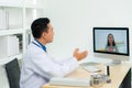 Asian man doctor wears white coat and headset speaking videoconferencing on laptop computer using online video call consultation