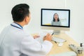 Asian man doctor wears white coat and headset speaking videoconferencing on laptop computer using online video call consultation