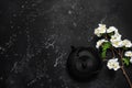 Asian metal teapot and blossom cherry branch artificial on a black stone background. Black cast iron teapot. Top view