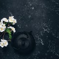 Asian metal teapot and blossom cherry branch artificial on a black stone background. Black cast iron teapot. Top view, square