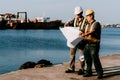 2 Asian middle-aged male engineers standing on the dock, helping to see the blueprints