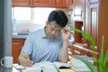 Asian middle-aged man sitting at desk at home, reading a book and studying