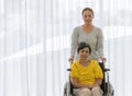 Asian middle-aged woman take carre and help older famale patient on a wheelchair with smile happy face