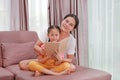 Asian mom and daughter reading a book on the sofa with looking at camera. Happy loving family at home Royalty Free Stock Photo