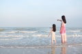 Asian mom and daughter relaxing on the beach on vacation. Mother pointing something with child girl looking in the sea. Back view Royalty Free Stock Photo