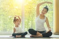 Asian mom practice yoga at home with a adorable daughter sitting next to her, trying to imitate the mother`s posture