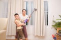 Asian mom and son having fun while cleaning up the room together with vacuum cleaner at home Royalty Free Stock Photo