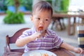 Asian 18 months / 1 year old toddler boy child sitting in high chair using fork eating whole cherry tomatoes