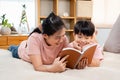 Asian mother and boy, wearing a pink t-shirt, The two of them lay comfortably on the bed, mother holding a playbook in her hand to Royalty Free Stock Photo