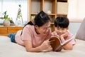 Asian mother and boy, wearing a pink t-shirt, The two of them lay comfortably on the bed, mother holding a playbook in her hand to Royalty Free Stock Photo