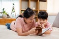 Asian mother and boy, wearing a pink t-shirt, The two of them lay comfortably on the bed, mother holding a playbook in her hand to Royalty Free Stock Photo