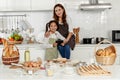 Asian mother and cute daughter, happy young mother teach cook together with small daughter doing bakery and learning computer and