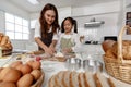 Asian mother and cute daughter, happy young mother teach cook together with small daughter doing bakery and learning to make cake