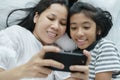 Asian mother and daughter playing game with phone together on the bed. Women and girl happy and fun in bedroom