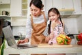 Asian mother and daughter preparing salad and using computer notebook. Leisure activity in a kitchen Royalty Free Stock Photo