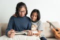 Asian mother and daughter read a book while sitting on the sofa. The little girl smiled and hugged his doll in the living room at