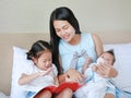 Asian mother with daughter and son read fairy tale. Female with her little children enjoying book indoors Royalty Free Stock Photo