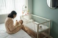 Asian mother embracing and playing with her baby son in bedroom. Young mom sitting on bed holding newborn child hands Royalty Free Stock Photo