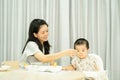 Asian mother feeding baby boy sitting on white highchair Royalty Free Stock Photo