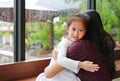 Asian mother and her daughter hugging with love near a glass window while raining day. Cute little girl looking at camera with Royalty Free Stock Photo