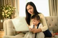 Asian mother holding her baby boy and working with laptop on couch at home Royalty Free Stock Photo