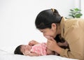 Asian mother holding and kissing newborn baby foot with love. Infant girl lying on bed at home and holding mom finger. Love and Royalty Free Stock Photo