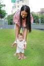 Asian mother learning her infant baby to walk first steps on the green grass garden Royalty Free Stock Photo