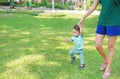 Asian mother learning her infant baby to walk first steps on the green grass garden Royalty Free Stock Photo